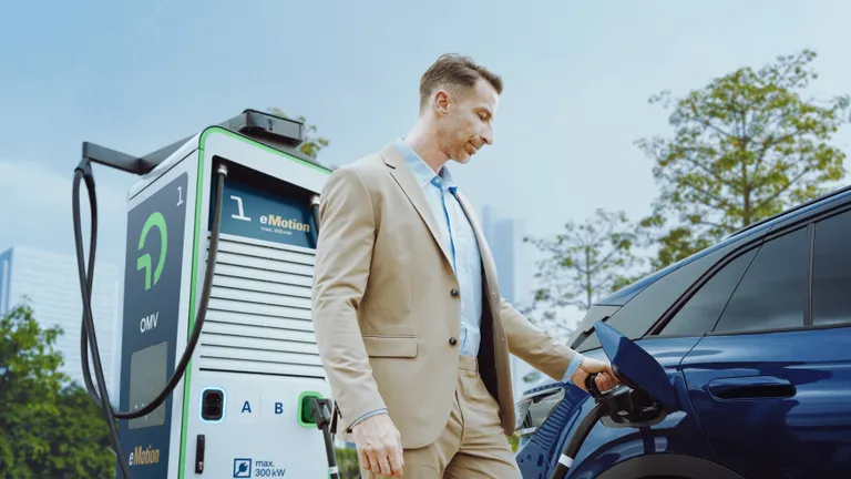 Férfi elektromos töltőnél tölti az autót.