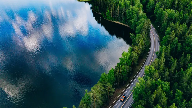 Tóparti út felülnézetből, amelyet erdősáv szegélyez, az aszfaltúton 2 autó közlekedik