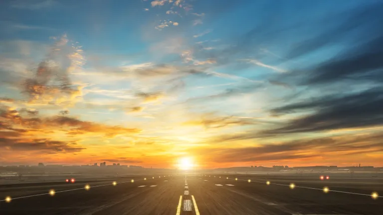 Leszállópálya aszfaltcsíkja, oldalról jelzőfények szegélyezik, a háttérben naplemente