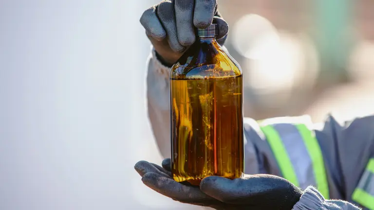 OMV üzemanyag minta közeli kép, amint egy dolgozó kezében, aki munkaruhát és védőkesztyűt visel
