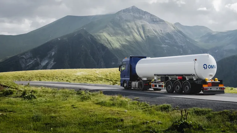 OMV tartályautó halad alpesi úton egy fennsíkon keresztül a hegyek felé